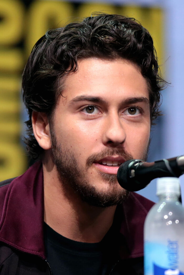 Nat Wolff speaking into a microphone at an event, showcasing his bio and career highlights in entertainment.