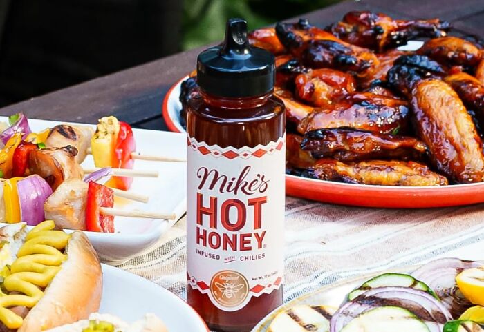 Bottle of Mike's hot honey with grilled chicken wings, skewers, and hot dog as gifts for person who has everything.