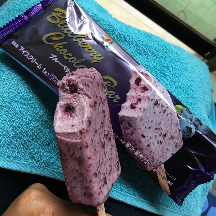 Partially eaten blueberry chocolate bar held by hand with packaging in the background on a blue towel, showing expectation vs reality.