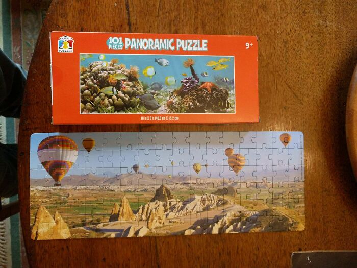 Partially completed panoramic puzzle of hot air balloons over rocky landscape contrasting box image of underwater scene.