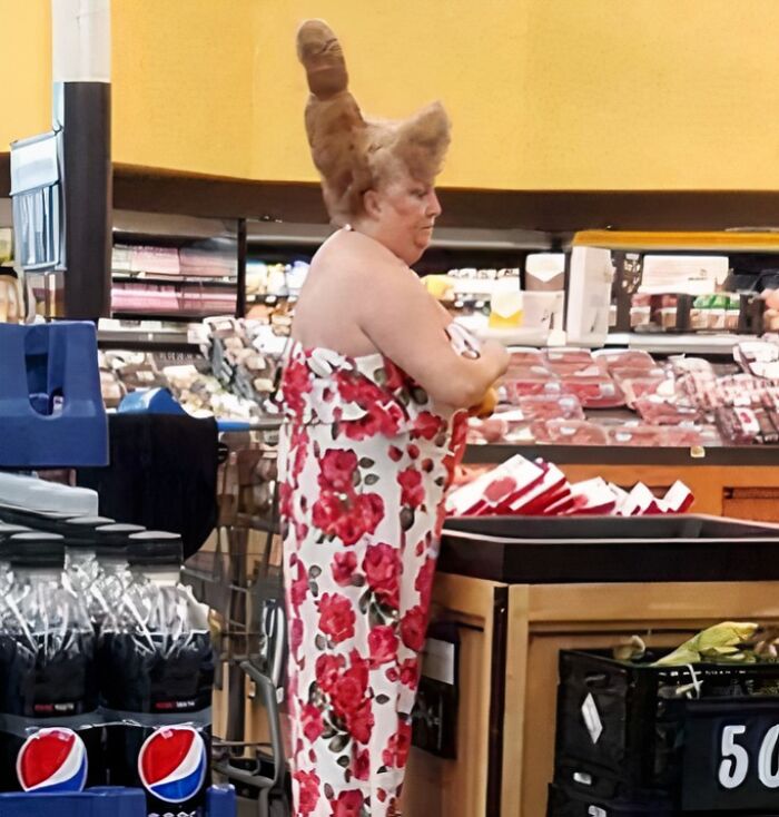 Woman with unusual bread-shaped hairdo shopping in Walmart deli aisle surrounded by meat products and Pepsi bottles.