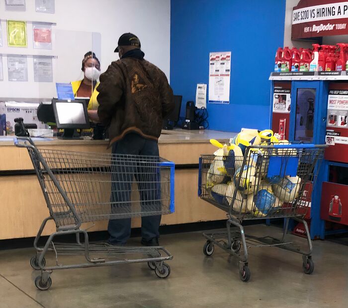 Customer wearing a brown jacket at Walmart checkout counter with full shopping cart and empty cart nearby indoors.