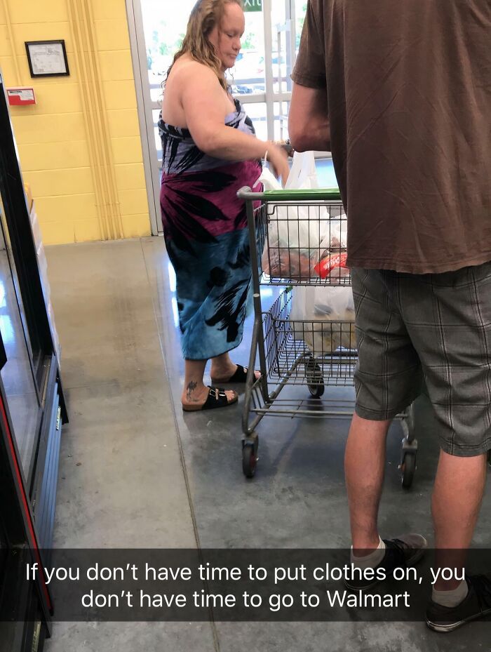 Woman shopping at Walmart in a towel dress, pushing a cart while a man stands nearby inside the store.