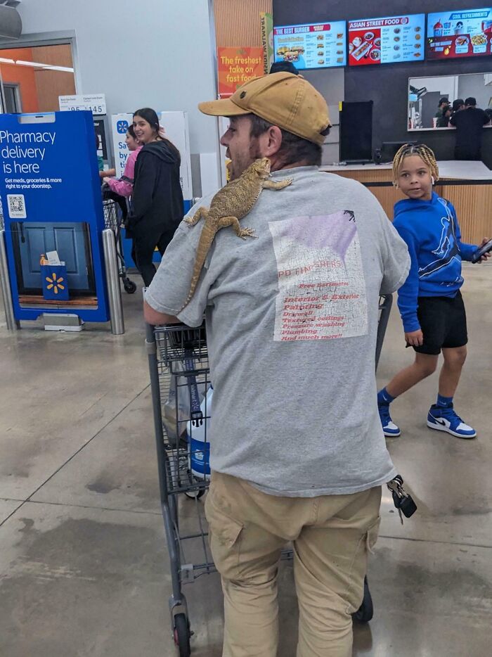 Man with a lizard on his shoulder pushing a cart inside Walmart, unusual scene from Walmart stores that might make you wonder.