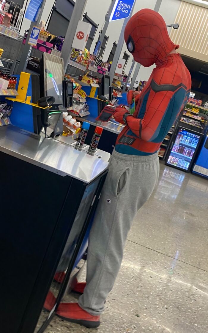 Person dressed as Spider-Man wearing sweatpants using self-checkout at Walmart store with snacks and drinks nearby