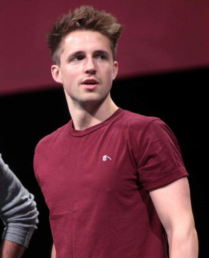 Marcus Butler wearing a maroon t-shirt, looking to the side during a public event or presentation on stage.