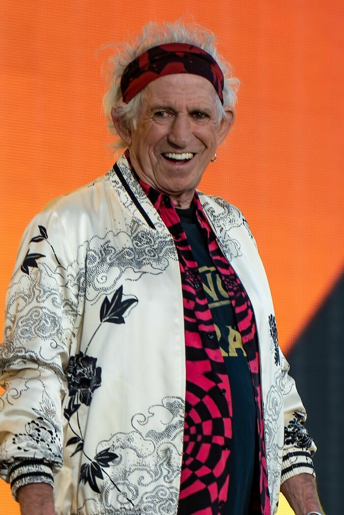 Keith Richards smiling on stage wearing a patterned jacket and red headband highlighting his music career.