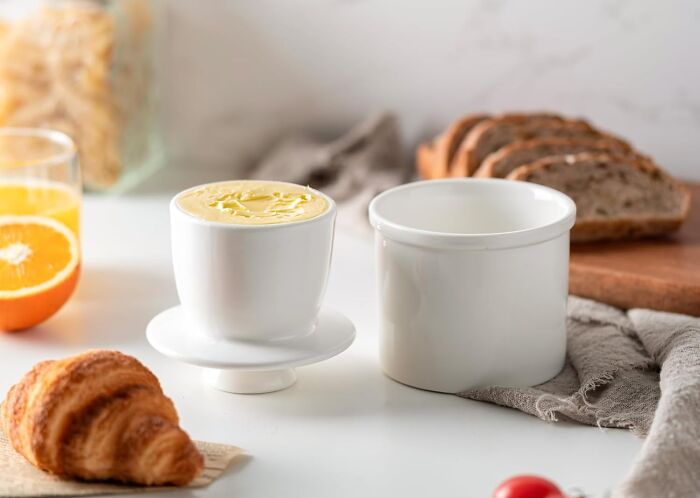 Host gifts concept with croissant, butter dish, sliced bread, and fresh juice on a white table setting