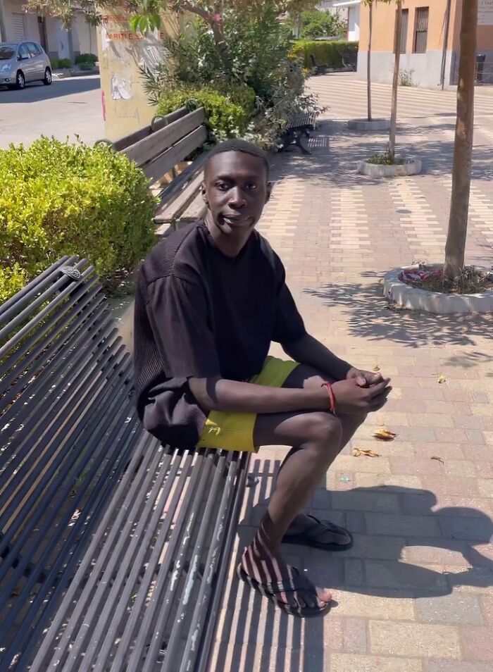 Young man sitting on a park bench outdoors, casual style, an internet icon who went viral randomly in public setting.