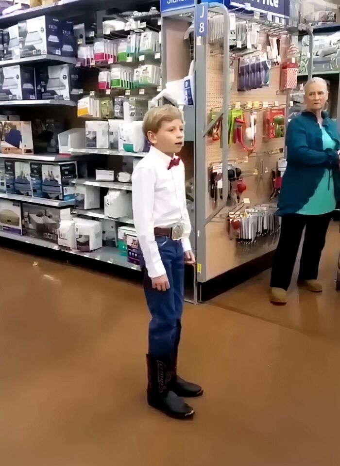 Young boy wearing cowboy boots and bow tie standing in store aisle, an unexpected internet icon in a viral moment.