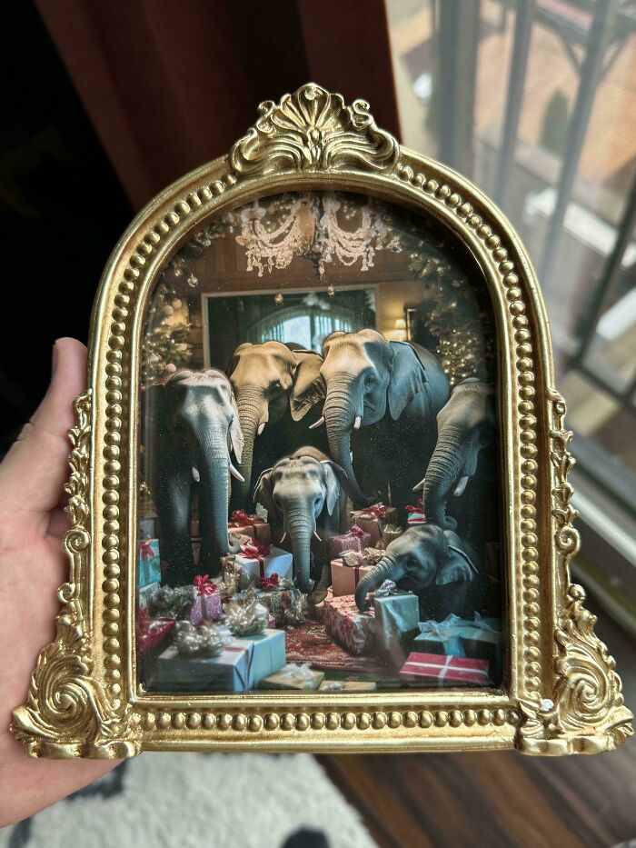 Hand holding a golden ornate frame featuring bizarre Christmas gifts with elephants surrounded by wrapped presents inside.
