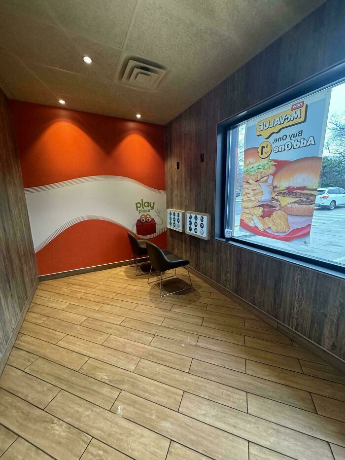 Empty fast food play area with wooden walls, tiled floor, and a large window showing an outdoor parking lot, liminal spaces.