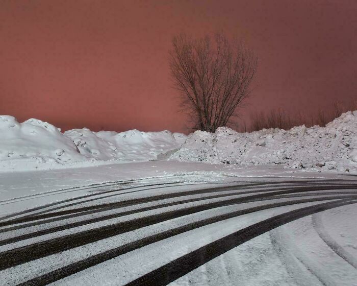 Snow-covered liminal space with tire tracks and bare trees under an eerie orange sky resembling the backrooms atmosphere