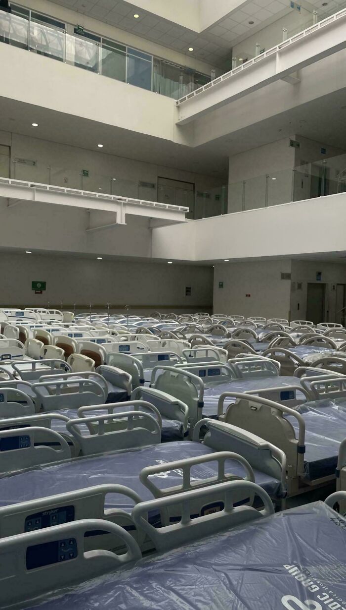 Rows of empty hospital beds in a large, sterile, liminal space resembling creepy backrooms atmosphere.