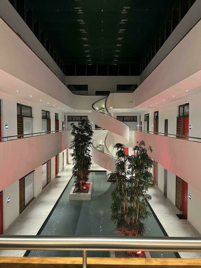 Modern empty building interior with spiral staircase and indoor plants in a liminal space resembling the Backrooms.