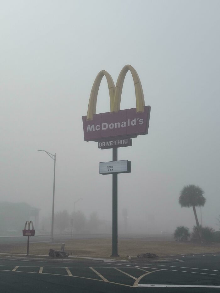 Foggy McDonald's drive-thru sign in a deserted parking lot, evoking creepy liminal space vibes like the Backrooms.
