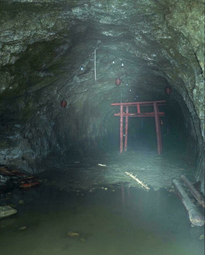 Dark cave tunnel with a red torii gate and hanging lanterns, evoking creepy liminal spaces like the Backrooms.