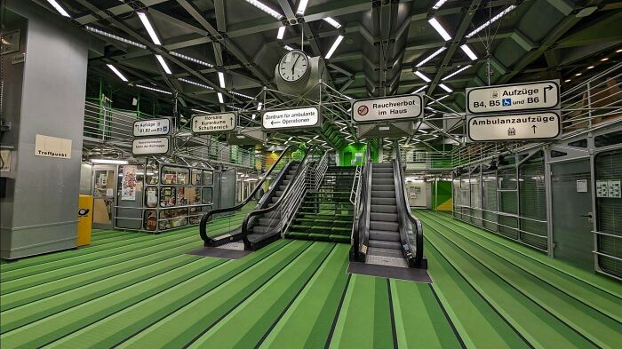 Creepy liminal space with green striped floors and escalators, resembling eerie empty backrooms environment.