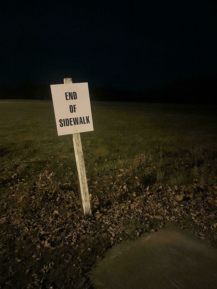 End of sidewalk sign in a dark, empty outdoor liminal space resembling backrooms atmosphere at night.