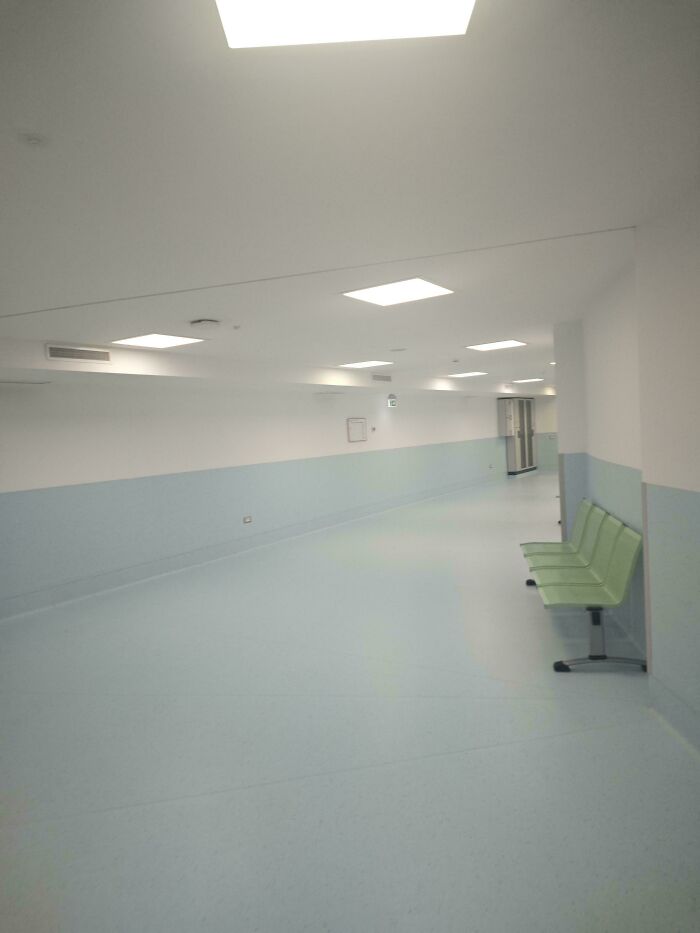 Empty hospital corridor with pale blue walls and green chairs, resembling creepy liminal spaces like the Backrooms.