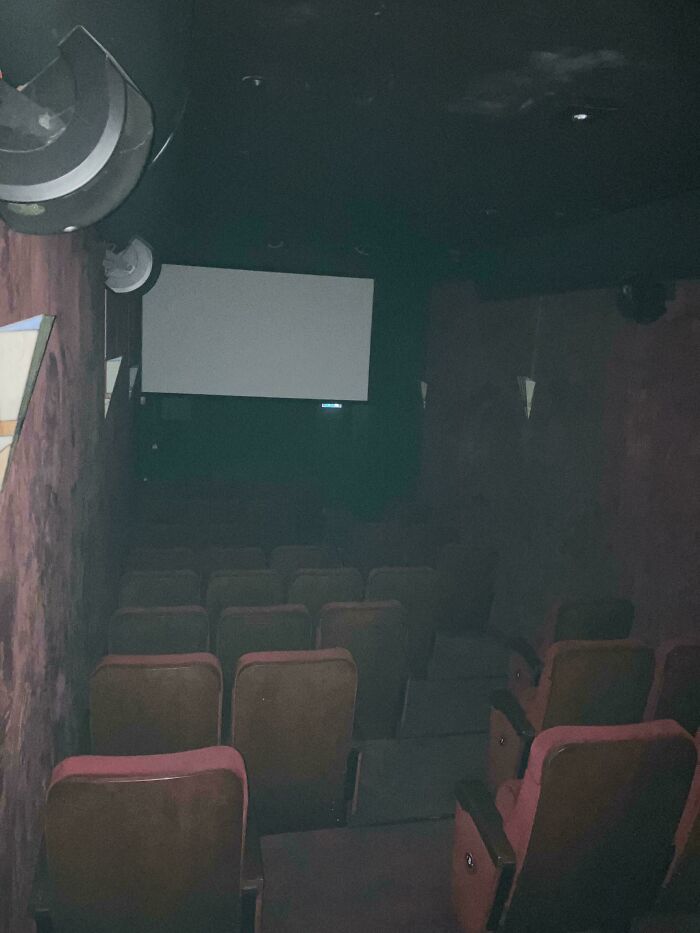 Dimly lit empty theater seats facing a blank screen in a creepy liminal space resembling the backrooms.
