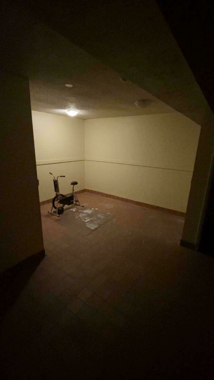 Dimly lit empty room with a single exercise bike, showing a creepy liminal space resembling the backrooms.