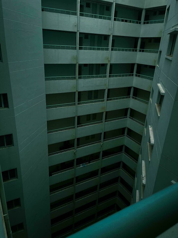 Dimly lit empty building corridor with repetitive railings and walls, evoking creepy liminal spaces like the Backrooms.