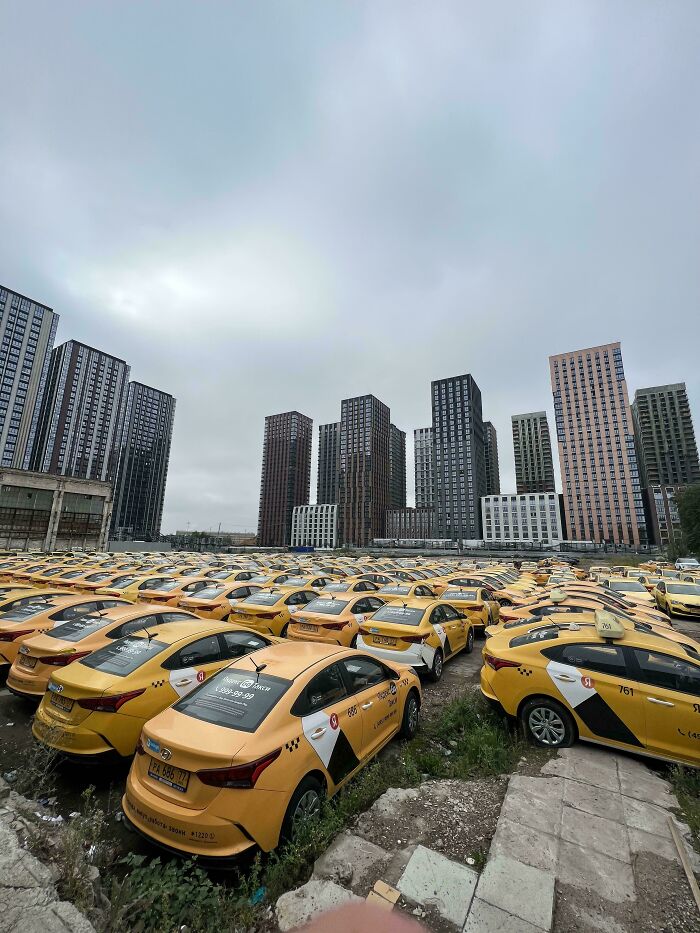 A vast parking lot filled with yellow taxis under overcast sky creating a liminal space vibe like the Backrooms.