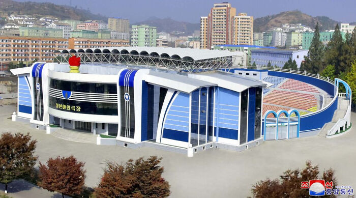 Modern stadium exterior in an urban area, resembling a liminal space with empty, eerie surroundings and distant buildings.