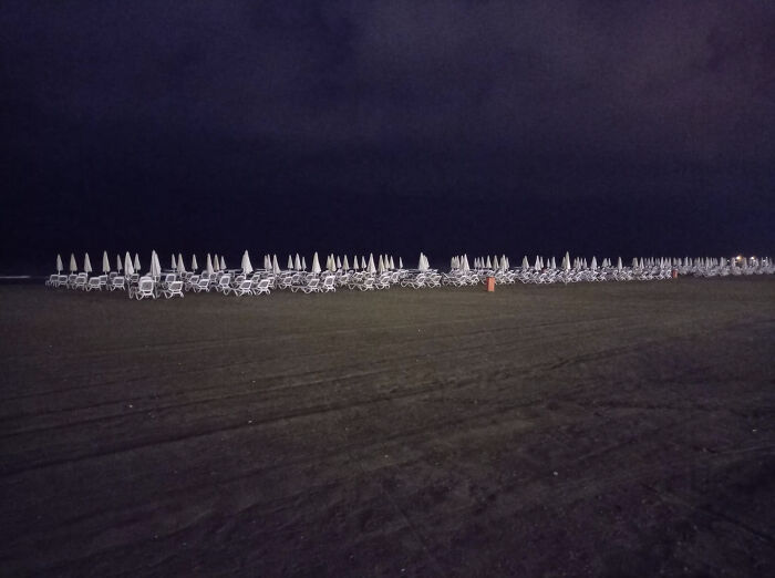 Empty beach chairs and closed umbrellas lined up in a dark, eerie liminal space that resembles the Backrooms atmosphere.