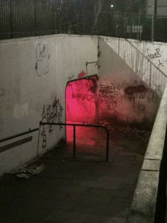 Graffiti-covered dimly lit liminal space with a red glowing entrance, creating a creepy backrooms atmosphere at night.