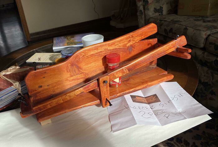 Wooden bizarre Christmas gift resembling a crossbow placed on a table with a note and household items nearby.