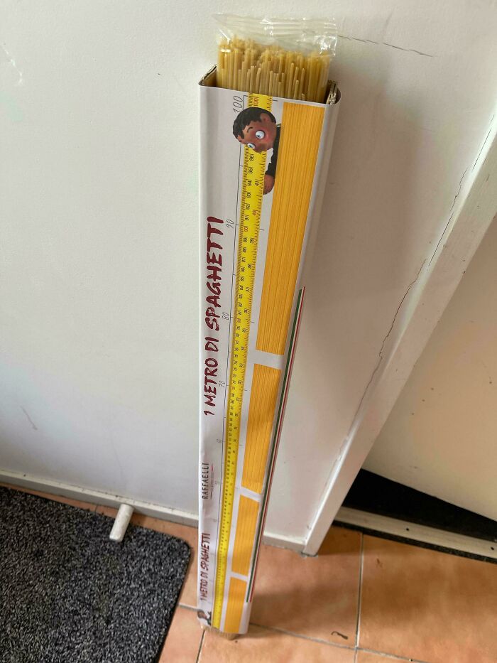 Long box of spaghetti labeled one meter of spaghetti standing against a wall among bizarre Christmas gifts.
