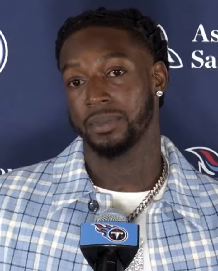 Calvin Ridley speaking at a press conference, wearing a plaid shirt and chain, with Tennessee Titans microphone visible.