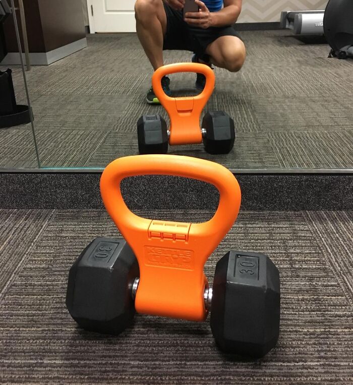 Orange kettlebell dumbbell on carpet with person reflected in mirror preparing to exercise apartment friendly fitness.