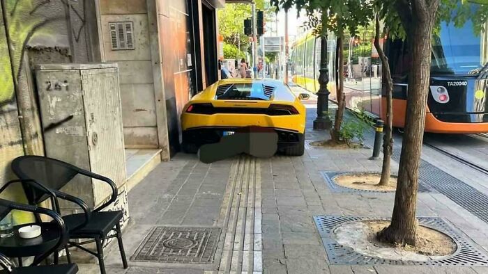 Yellow sports car parked on sidewalk blocking tactile path beside cafe, a clear example of next-level jerks in city street