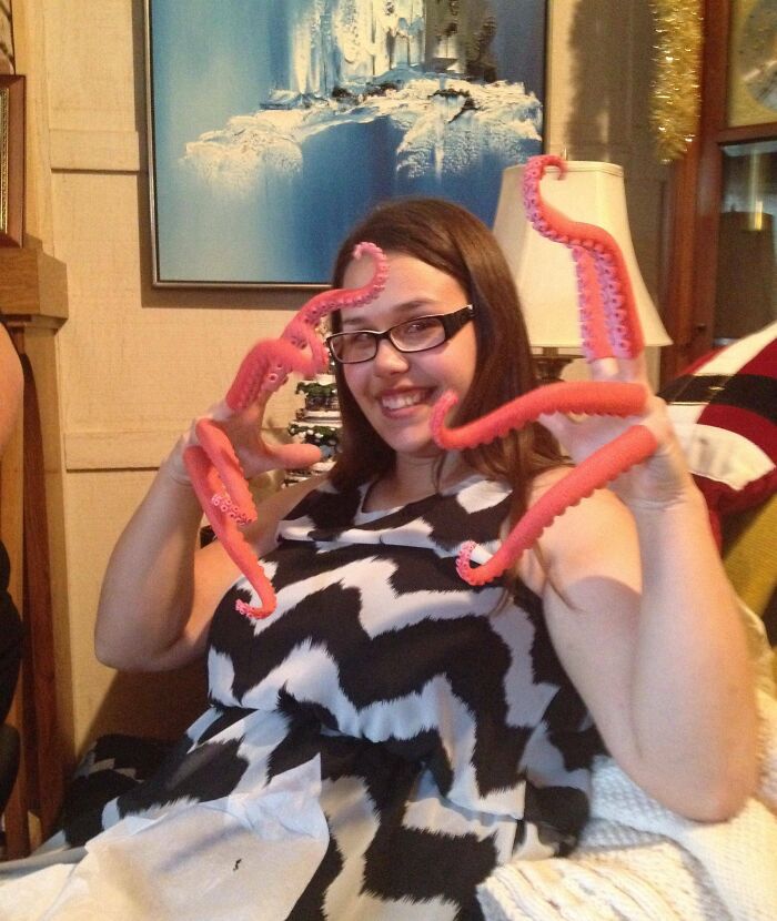 Woman smiling indoors wearing novelty pink octopus tentacle gloves as bizarre Christmas gifts received by people.