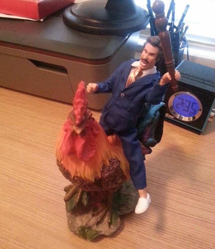 Action figure riding a colorful rooster, one of the most bizarre Christmas gifts displayed on a wooden desk.