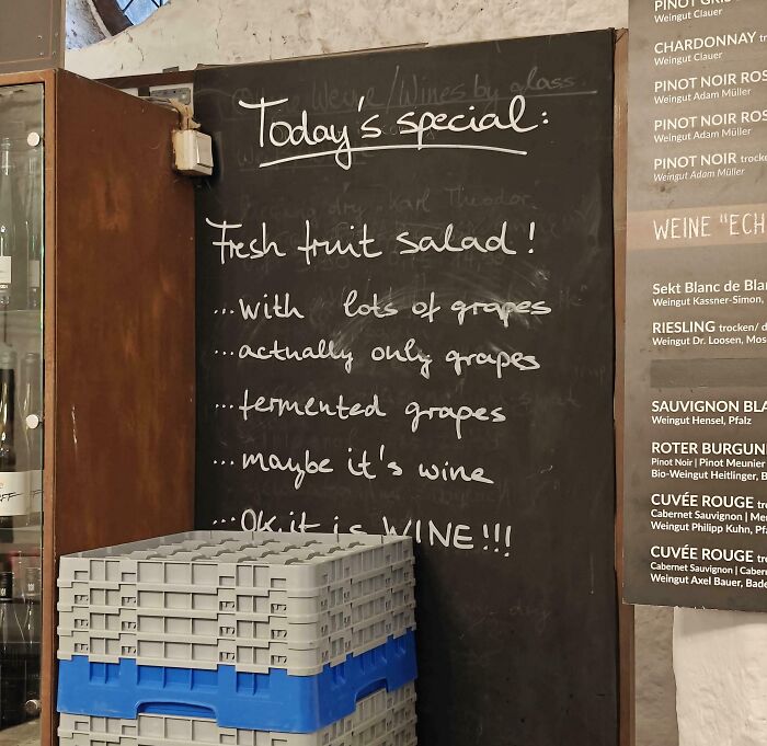 Chalkboard with humorous wine menu listing fresh fruit salad as fermented grapes and wine, capturing 2025 funny pictures weirdness.