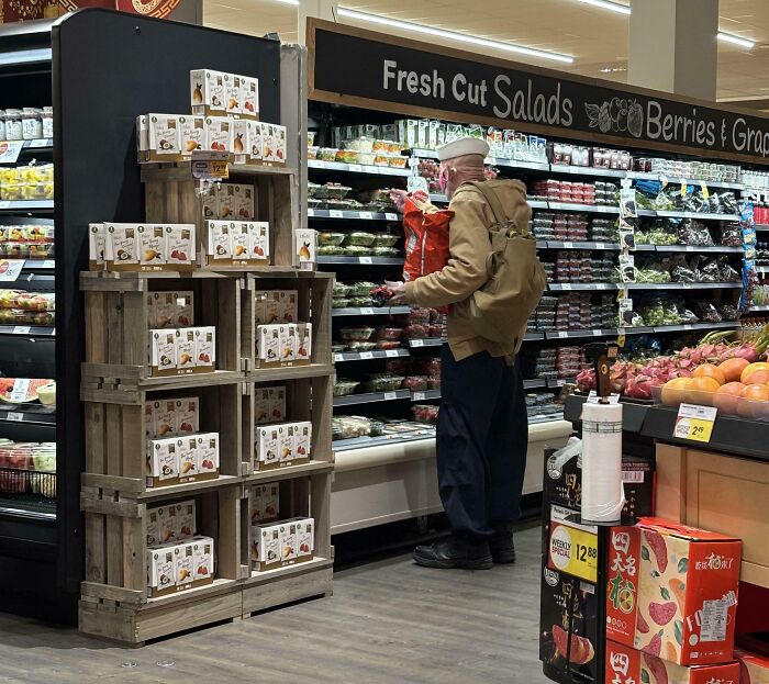 Elderly man shopping for fresh cut salads and berries in grocery store, capturing funny pictures from 2025 weirdness.