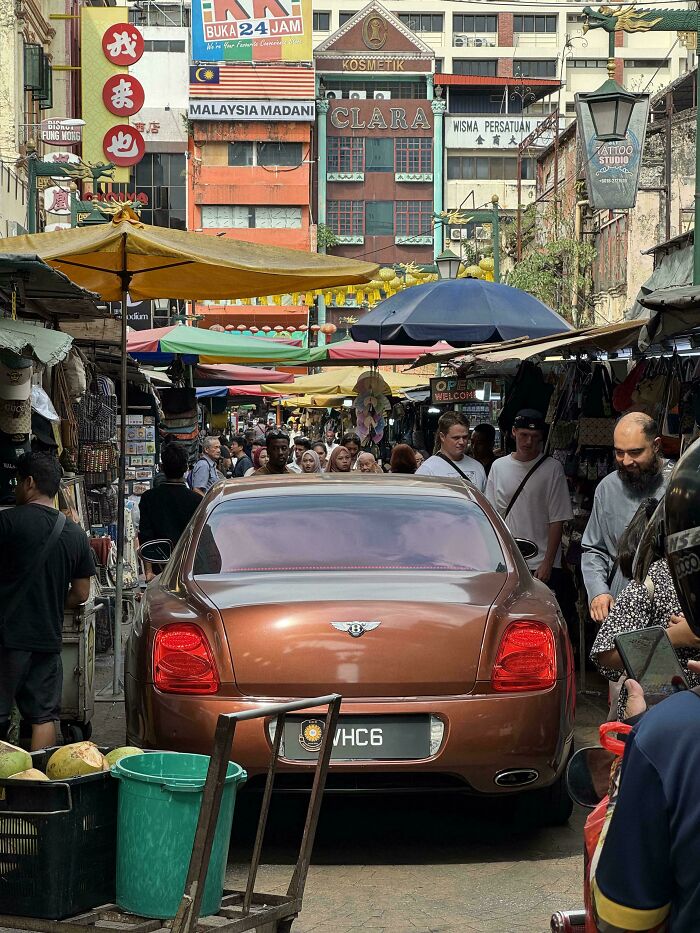 Luxury Bentley driving through crowded street market, shoppers squeezed aside — next-level jerks causing chaos.