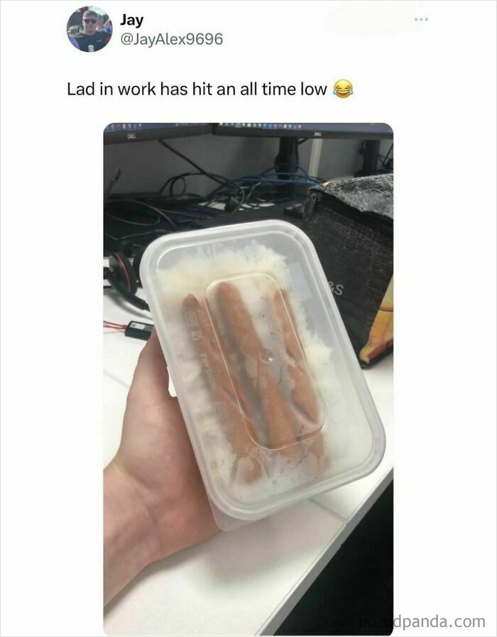 Hand holding a food container with two sausages and rice, a funny food meme about low lunch expectations at work.