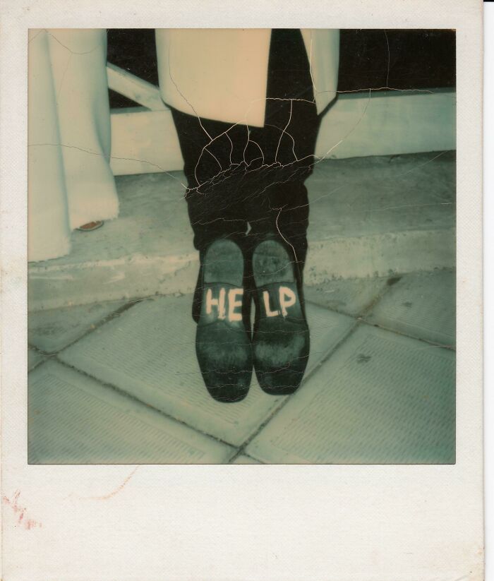 Person wearing black shoes with the word HELP written on the soles, capturing a fun sibling moment outdoors on tiles.