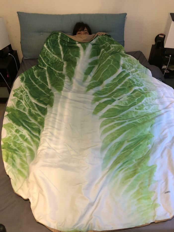 Person wrapped in a fun lettuce leaf blanket on a bed, showing how life is more fun with siblings moments.