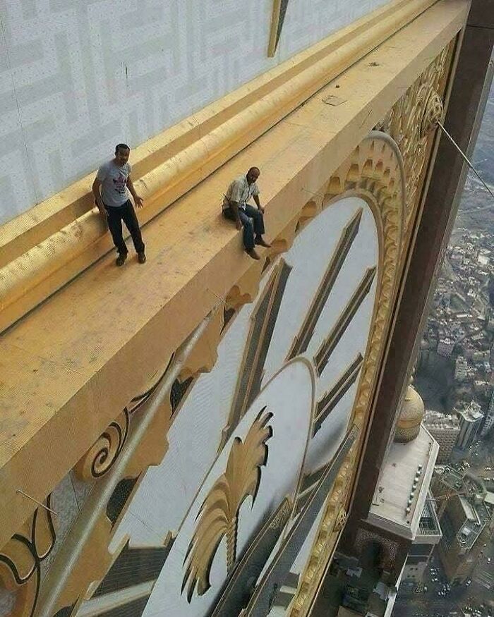 Two men sitting and standing on the edge of a giant clock face high above a city, an interesting and daring view.