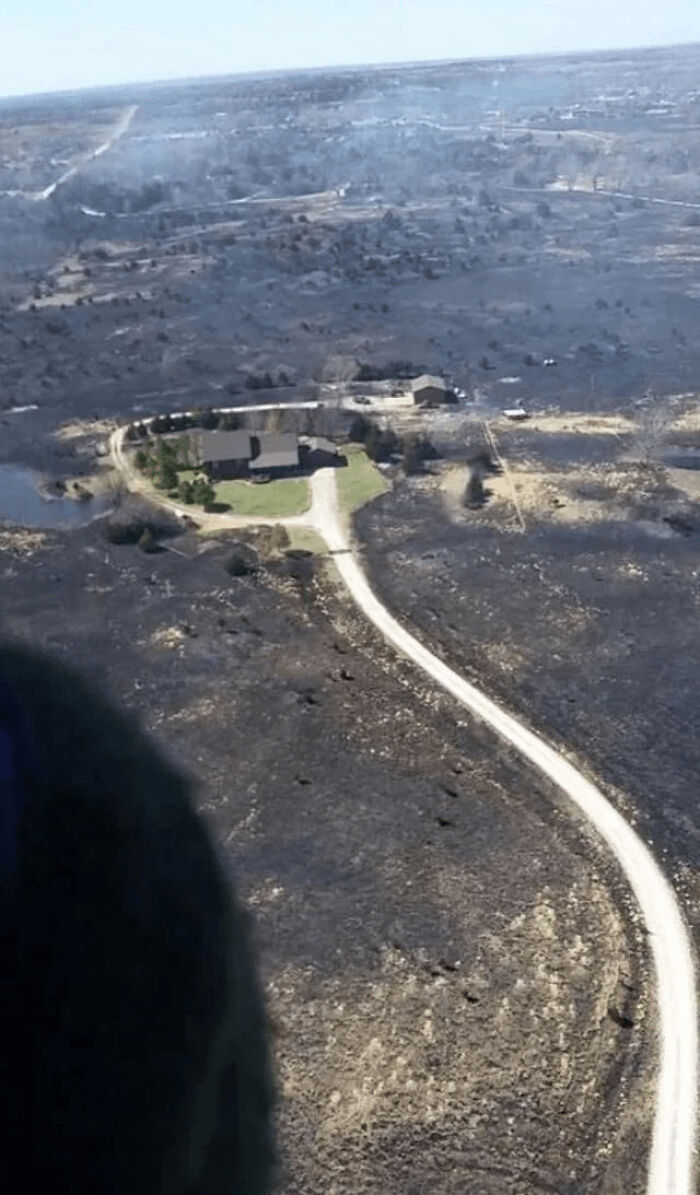 Aerial view showing a house untouched by fire, surrounded by burnt land after a large wildfire incident.
