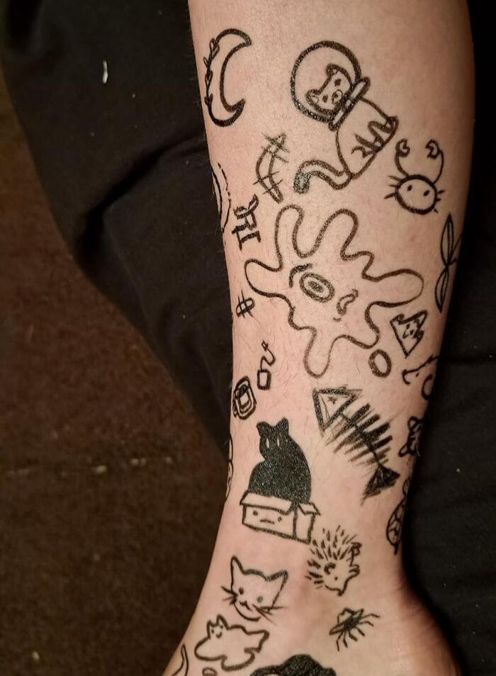 Tattooed arm with various black ink doodles including cats, a moon, and abstract shapes illustrating best sellers and delusional trends.