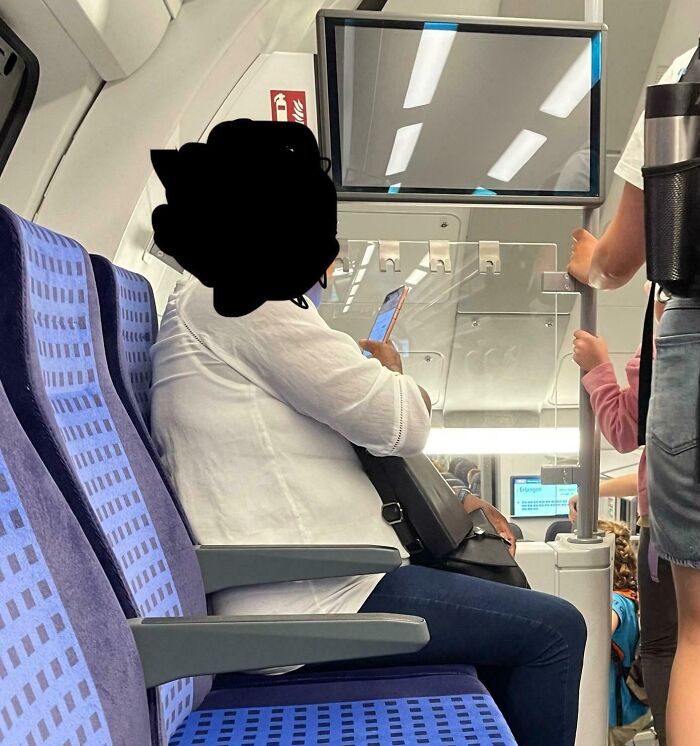 Seated passenger with large bag hogging a train seat and blocking aisle, example of next-level jerks