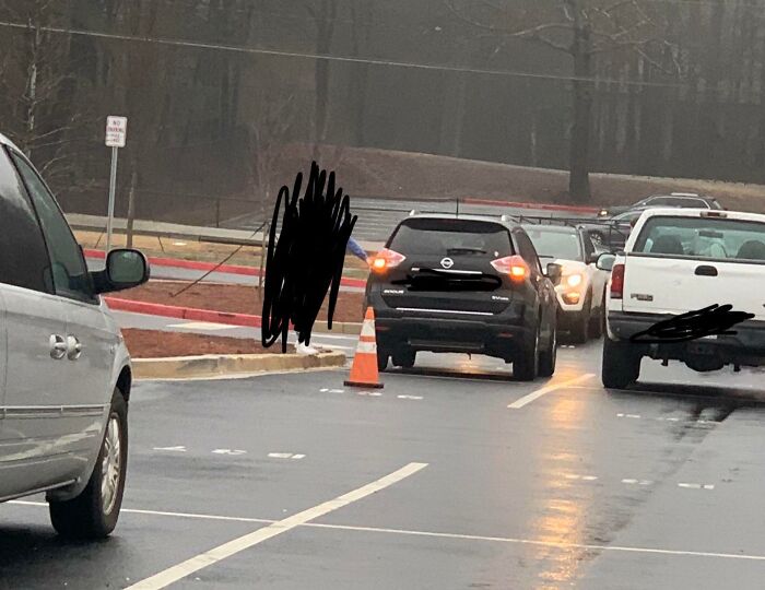 SUV blocking lane in wet parking lot beside traffic cone, rude parking behavior illustrating next-level jerks