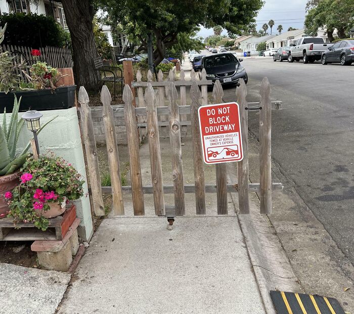 Wooden gate across sidewalk with Do Not Block Driveway sign, parking obstruction by next-level jerks